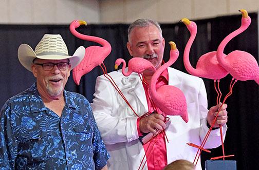 Jason Schneider, Memorial Foundation board chairman, holds some of the bright pink flamingoes sold during Friday’s Miami Vice Gala at the fairgrounds. At left is auctioneer Kelly Kliewer.
