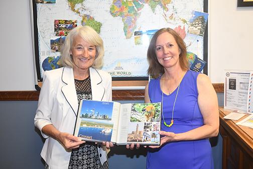 Jan Dick (left) and Wendy Dethlefs stand in front of their map that showcases where residents have traveled and features postcards that have been sent to them. They have received so many that the rest are kept in an album. News-Register/Jeni Moellenberndt