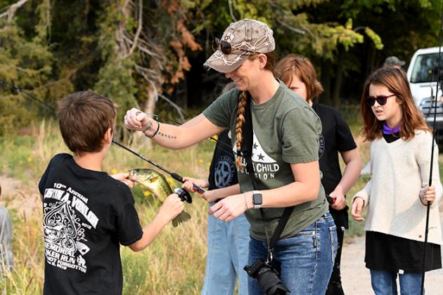Heather Vanloh, who lost her husband years ago while he was in the military, helps youth during a fishing expedition Friday at Timberlake Ranch Camp.