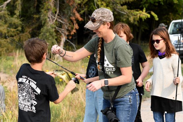Heather Van Loh, whose military husband died several years ago, helps young members of A Soldier’s Child Foundation fish during a weekend outing at Timberlake Ranch Camp.