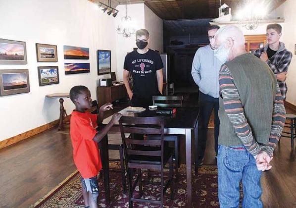Featured artist Ernie Ochsner (front right) discusses his process with aspiring fellow artist, Jordan Ramaekers (front left) while his family members Preston, Ryan and Ethan Ramaekers listen in. (News-Register/Jeni Moellenberndt)