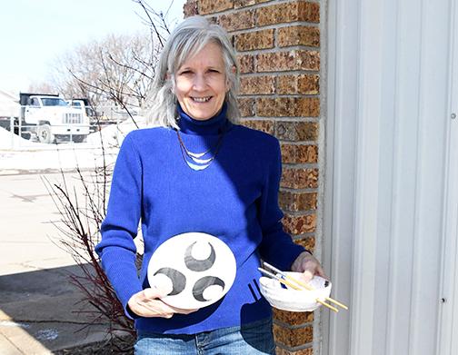 Mardell Jasnowski stands with plates and rice bowls that she created in her pottery studio.