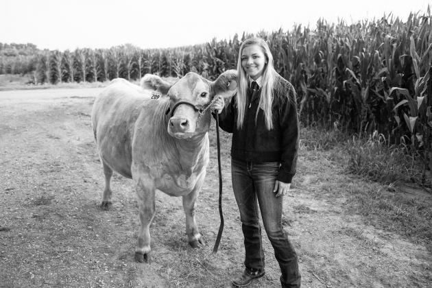 Donning her FFA jacket, Emma Snoberger stands with one of her cows in her family’s field.