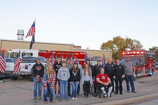 Members of the Aurora Flag Friday group were surprised by Aurora fire and EMS personnel last week. Together, first responders and students included, front row, from left: Zaiah Anson, Darren Friesen, Victoria Shirley, Jennifer Slocum and Caspian Walters. Back row from left: Connor Smith, Matthew Luddington, Ethan Jones, Jalen Daugherty, Daniel Slocum, Chris Damron, paramedic Matt Hedge, firefighter Kirt Smith, paramedic Sara Newton and Gage Anderson. 