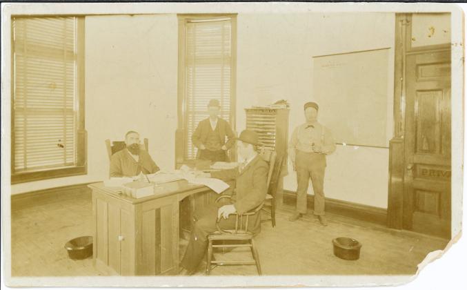 Located at a familiar site, the Hamilton County Courthouse, this photo was taken in the 1895-96 era. It captures Sheriff A. J. McConaughey sitting at his desk (far left) across from his son, and deputy, B. E. McConaughey. Also pictured is janitor Charles Davis (far right). The fourth man, located in the back, is unknown.