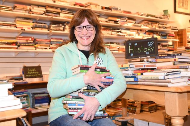 Susan Williams craddles a stack of used books in her downtown store, explaining a strategy to revamp her business model in hopes of getting more donated books into the hands of people who need them.
