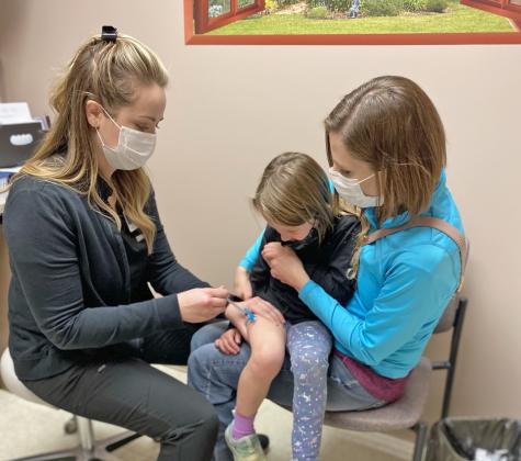 Courtesy photo // Aria Heiden sits bravely on her mother Jennifer’s lap as she receives her first shot of the Pfizer vaccine for children from nurse Ashley at Memorial Health Clinic in Aurora.
