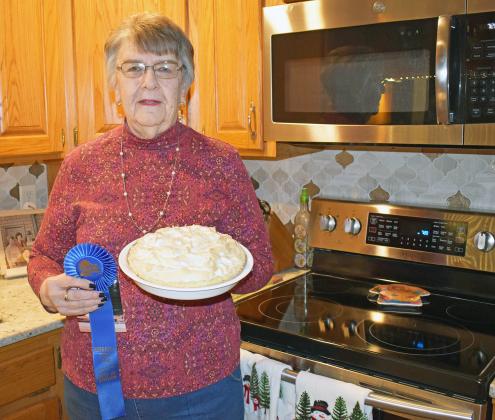Berniece Luthy stands in her kitchen with her blue-ribbon worthy raisin sour cream pie. The blue ribbon pictured showcases just one of her Best of Division finishes at the Nebraska State Fair, where Luthy is also a volunteer.