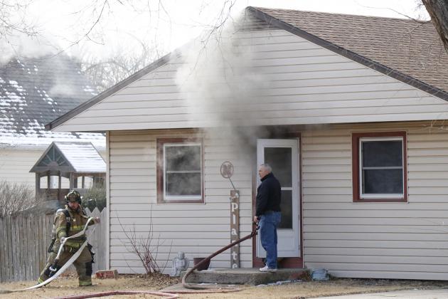 Aurora Fire Chief Tom Cox holds open the door for firefighters to run a hose into the smoke-filled home on 7th Street Friday morning.  