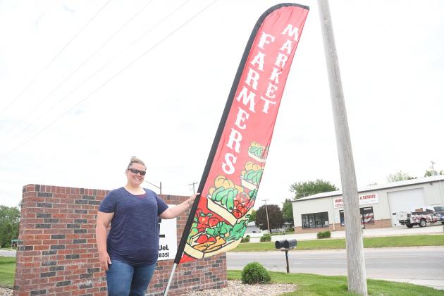 Organizer Vicki Hill holds up the farmer’s market banner on Highway 14. The banner is near where it will be when the Tuesday market opens up on June 7. 