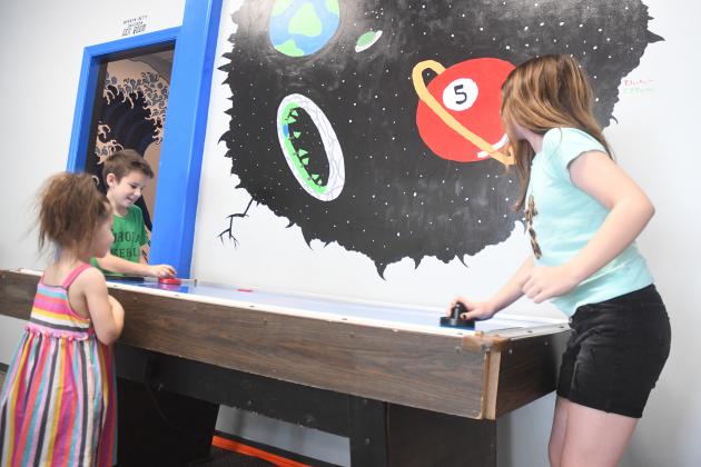 Madison, Conner and Natalie James play air hockey next to the mural that won the contest last month with the “Great Wave” mural in the neighboring Merwyn and Betty Davidson Zen Room. 