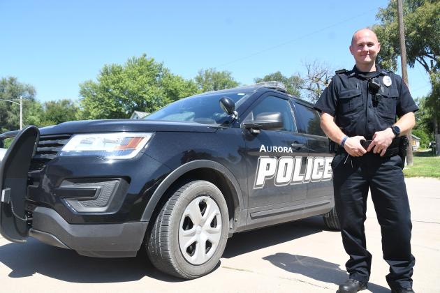 Police officer Cody Barry poses alongside an Aurora Police Department cruiser near the Law Enforcement Center Friday. Barry is the newest officer to join APD.