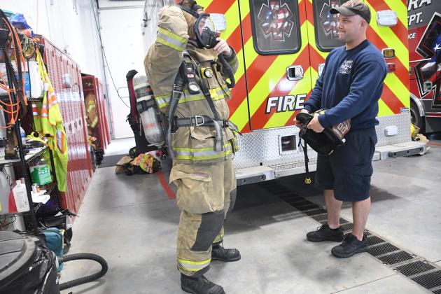 Volunteer Nolan Forbes puts on his bunker gear with the newly transferred self-contained breathing apparatus while EMS Supervisor Tanner Greenough looks on.