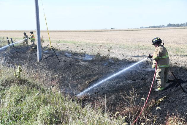 Aurora volunteer firefighters continue to hose down the area of a ditch fire after putting the flames out near the intersection of 11 and M Roads on Thursday. The fire was caused by a sparking transformer, according to Aurora Fire Chief Tom Cox.