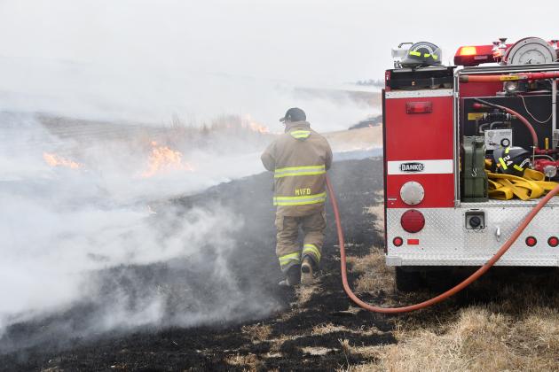 A Marquette firefighter uses a hose from a fire truck to put out flames in a ditch fire along Highway 14 Tuesday morning. Marquette firefighters also responded to a fire at a barn on North S Road Friday.