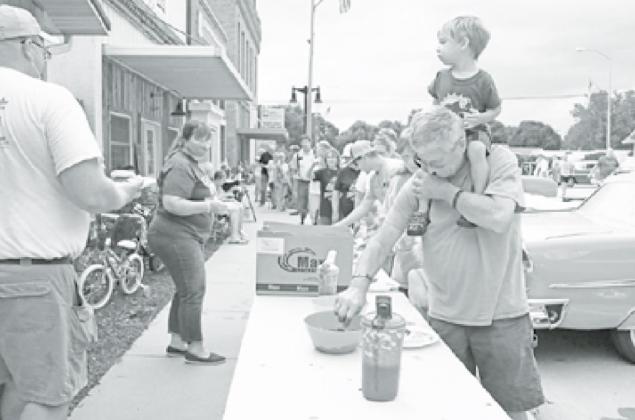 Hampton Public Schools staff members Joel Miller (left) and Jan Ediger help to pass out free BBQ pulled pork meals to the public, courtesy of the Roger Bamesberger family. The line stretched down the block. News-Register/Cheyenne Rowe
