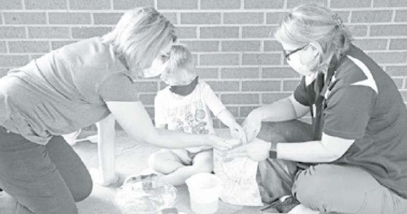 MCHI Ocupational Therapist Kim Eberly (left) helps young Knox Sabata explore his sandy activity. MCHI Occupational Therapist Carla Christenson also encouraged the young Auroran to squish the material between his fingers. News-Register/Cheyenne Rowe