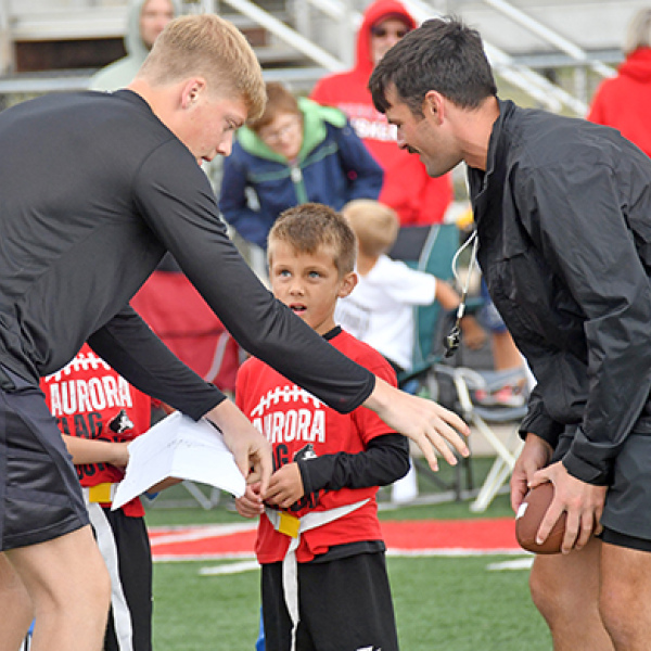 First grader Elijah Driewer receives some quarterback handoff advice from former Aurora QB1 Ethan Shaw (right) and his coach, Maddex Dummer.