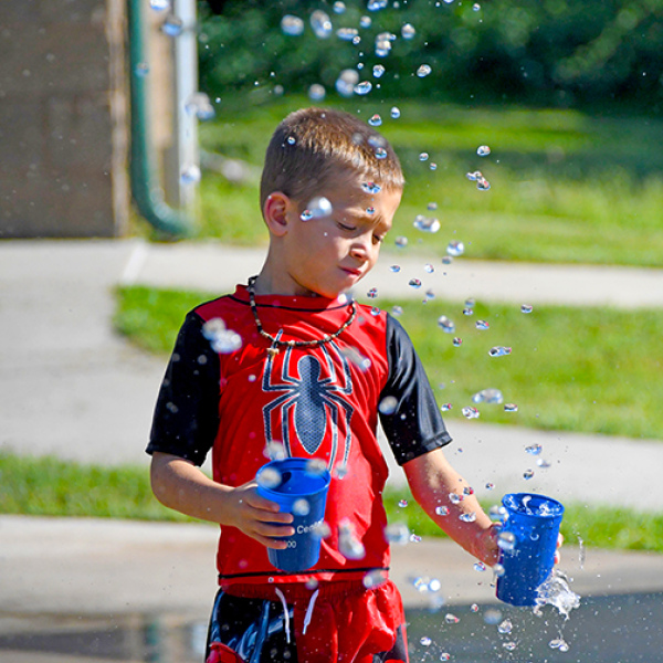 Luke Janzen fills up cups with water from the splash pad’s fountains during his family’s visit in the Thursday afternoon heat. The splash pad in Cole Park is now closed for the season.