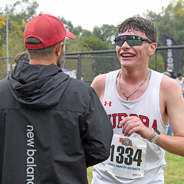 Grayson Oswald shares a moment with Aurora coach Tony Sigler after becoming the champion runner in the C4 district last week. Oswald laughs over how he broke his shoe during the second half of the race.
