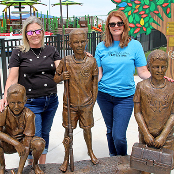 Julie Hoffman, left, and April McDaniel are pictured outside the Peyton Parker Lane Playground in York next to statues of their late sons for whom the inclusive playground is named. The women and their husbands were members of the group that founded the facility which opened in 2023. 