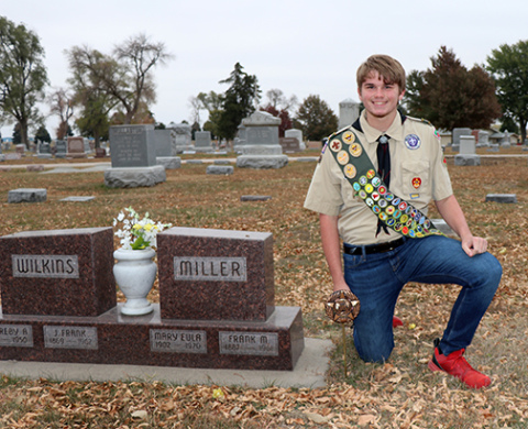 Astin Kennedy kneels next to one of the many markers that he placed in the Aurora Cemetery as part of his Eagle Scout project.