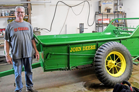 Gary Andrews stands with his current project, a John Deere wooden manure spreader.