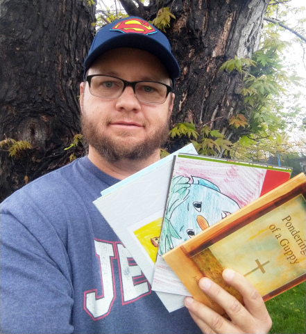 Josh Salmon stands with the two children’s books he has written and his newest creation, a book of poetry.