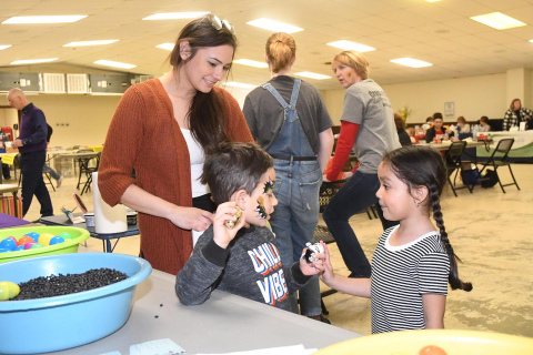 Melanie Dominguez (right) gives Attikus Louela a small plush tiger at the Early Childhood event  while his mother watches. Louela had just completed an egg shaker, which he holds in his left hand, when Dominguez gave him the toy.