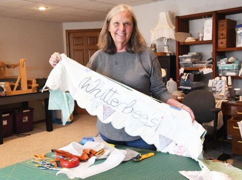 Kelly Elge holds up the sign of her business, Whitterbees, a work in progress made of parts from used quilted blankets. Elge named her crafting enterprise after a niece who showed her how to make blankets into jackets.