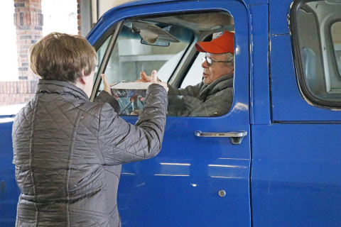 Aurora Senior Center volunteer Pat Phillips (left) hands a hot meal to Bob Dudley last week at the center’s meal drive-thru.