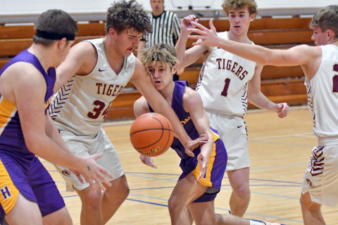 Hampton’s Jack Bullis (middle) tries to go between three East Butler defenders while trying to get the ball to teammate Korbin Stump in the Hawks’ 57-33 loss to the Tigers Saturday. 