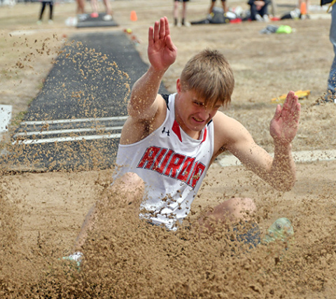 Aurora senior Carsen Staehr crashes into the sand pit during his final run through the long jump event, winning by half an inch over second place at Friday’s home invite. 