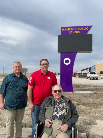 Pictured from left in front of the new Hampton school sign on Highway 34 are Kevin Wall of Hampton, Mike Wall of Forney, Texas and Denny Wall, who now lives in York. Denny and his wife Beverly donated funds to launch the sign project.