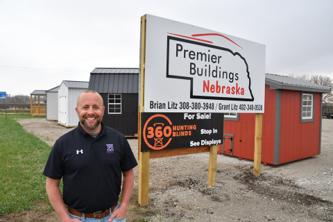 Co-owner of Premier Buildings Nebraska Brian Litz stands near some buildings and his sign on North W Road near Hampton. He joined with his cousin Grant a year ago to sell buildings, trailers and deer blinds straight off his lot.