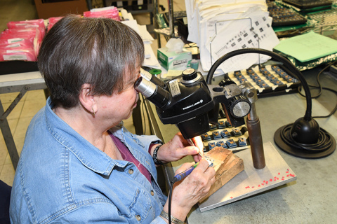 Carol Schenk looks through a microscope, part of a job she has enjoyed for almost all of the company’s 50-year history.