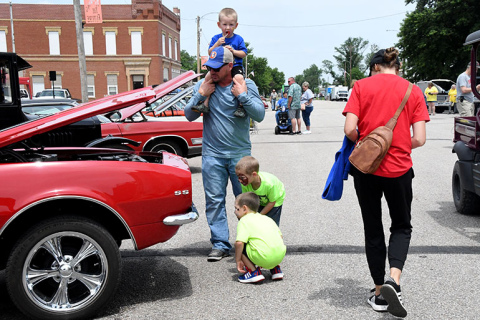 The Harmons, including father Jacob, Jackson on his shoulders, Garrett with dog face paint and Kaiden, kneeling, inspect a vintage automobile at Giltner Daze Car Show.