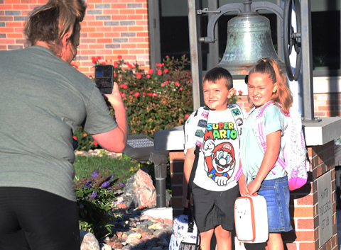 From left, mother Jenny Goertzen eagerly takes a photo of her children, Chance (1st grade) and Kendall (3rd grade), in front of the Hampton school bell on the first day of school Aug. 16.