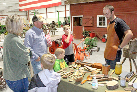 Barbie and Clint Mickey with their sons Creighton and Corbin and friend Emerson Myers discuss the process of wood carving with spoon carver Alex Brechbill on Sunday in the newly renovated Wesley Huenefeld Agricultural Museum during Day on the Farm on Sunday. 