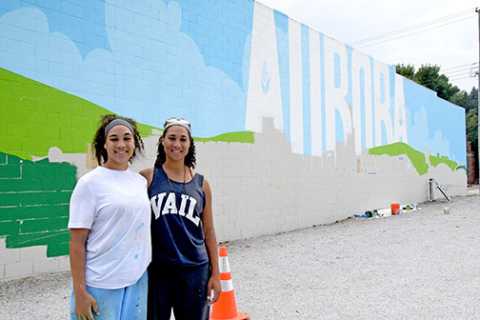 Artists Bristol, left, and Brianna Lewis stand next to the mural they are creating in downtown Aurora for the Hamilton Community Foundation.