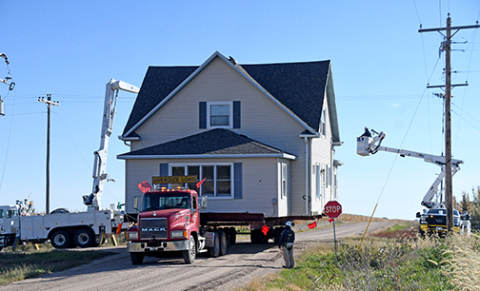 Utility crews lift power lines to allow the Oswald house to pass under