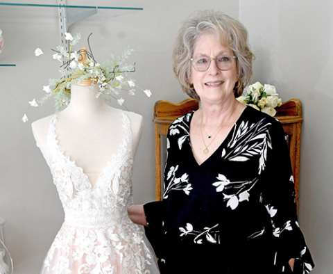 Dream Designs Bridal Shop owner Deanna Powell stands next to one of the nearly 800 dresses in her shop. She recently learned that the building her shop has occupied for over 20 years was built by a seamstress at the turn of the 20th Century.