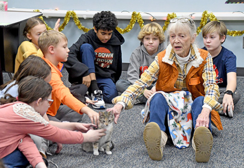 Aurora Adopt-A-Pet volunteer, Cathy Paule (right), talks to 5th graders about Adopt-A-Pet and how they can help the pets there as well as their own animals. At center is shelter kitten, Mimsey, who was brought to show the students as they celebrated the 20th season of  the Christmas Cheer class fundraiser. 