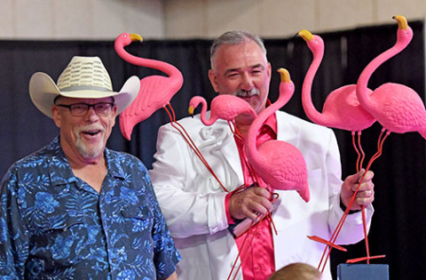 Jason Schneider, Memorial Foundation board chairman, holds some of the bright pink flamingoes sold during Friday’s Miami Vice Gala at the fairgrounds. At left is auctioneer Kelly Kliewer.
