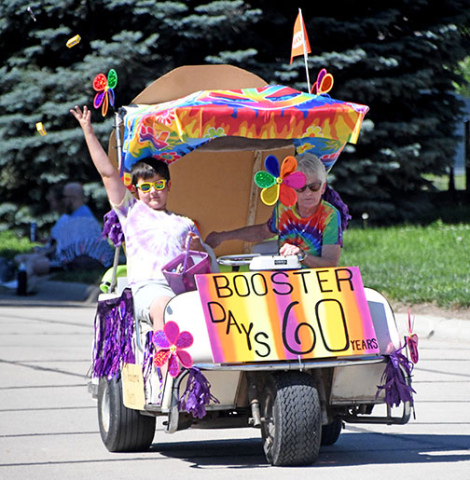 Damaris Olsen and her grandson, Reid, throw out candy to the crowd as they ride in the Booster Days Parade in their entry which won the award for Best Theme.