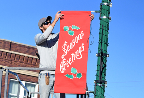 City crew member Riley Nuss hangs a Christmas banner on Aurora's downtown square