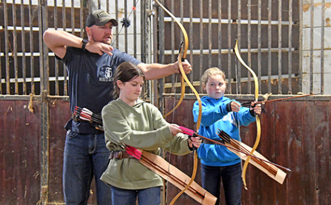 Great Plains Mounted Archery instructor Chris Patton shows his students, Londyn Ommert (left) and Penelope Mann how to adjust their bows for better aim. 