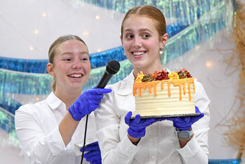 Makenna Oswald and Jasmine Hansen encourage guests to bid for one of the decorative cakes made for the Harvest Gala’s dessert auction Saturday night.