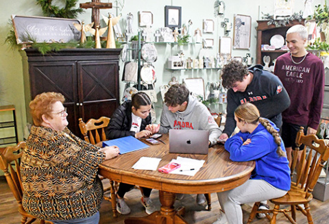 Angie Wall, left, owner of Honeysuckle Lane, watches as students from the Aurora High School marketing class work on a social media campaign to promote the store’s fall and Christmas sales and events. The students pictured are, from left, seated, Morgan Calkins, Parker Smith and Paityn Wyatt. Standing at right are Keegan Cheney and Jace Dorsey. 