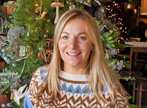 Belgian Marie Brasseur, an exchange student to Aurora in 1997-98, poses by a Christmas tree in the window at the Old Homestead Market and Floral during her visit here last month. She recalls with fondness the Christmas she spent here with one of her host families. 